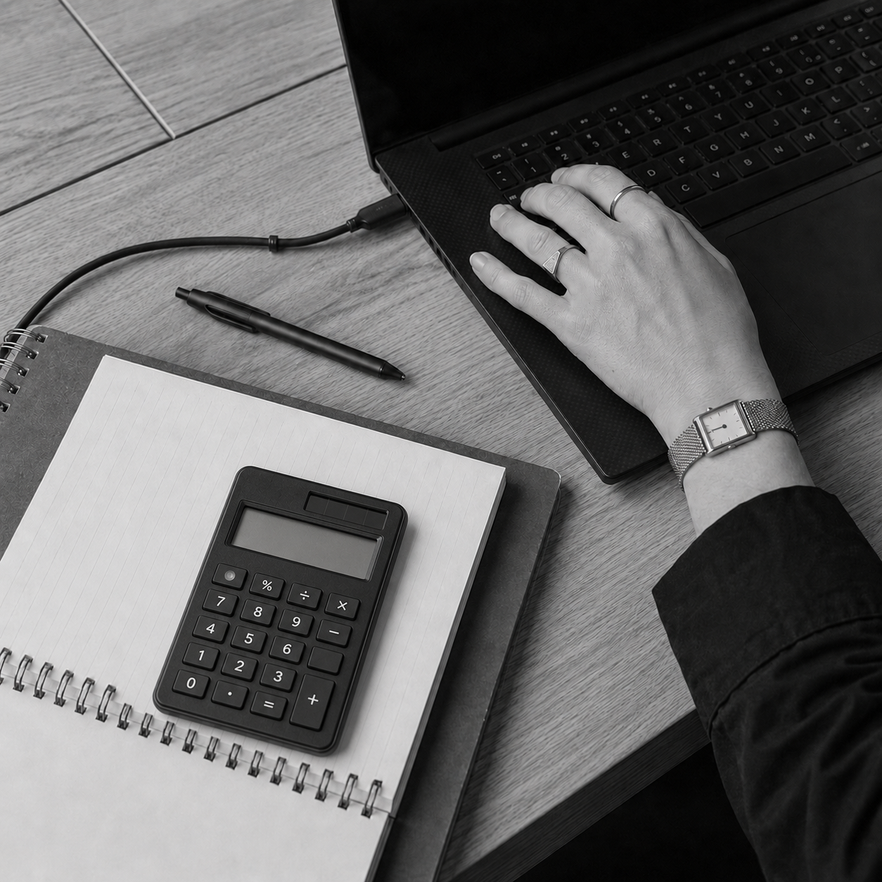 Overhead view of a hand typing on a laptop next to a calculator and notebook