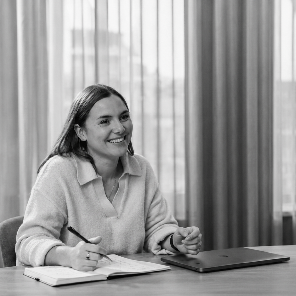 Woman smiling while writing in a notebook at a table with a laptop