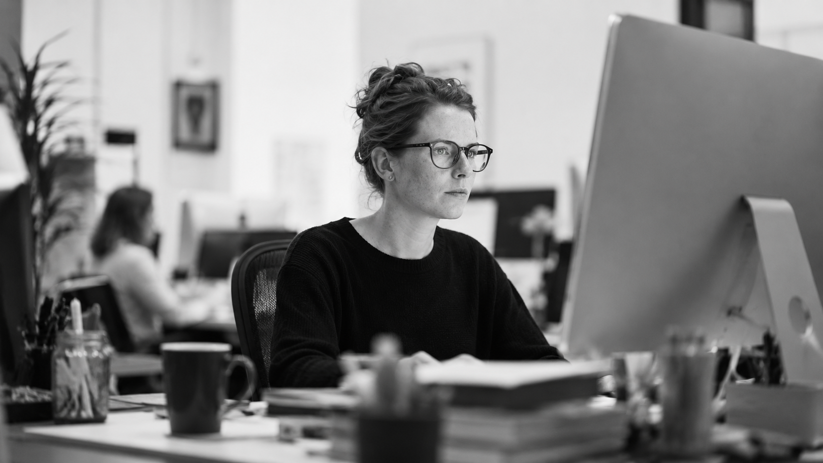 Black-and-white image of a professional focused on a desktop computer in a modern office.