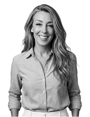 IncWorx consultant, Suzanne, smiling in a grey collared shirt and white slacks, hands in her pockets.