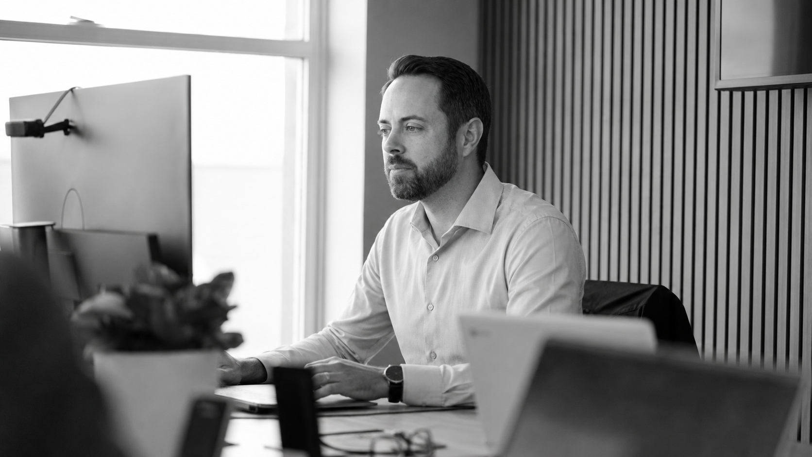 Technology consultant working at a desktop computer in a modern office with a focused expression.