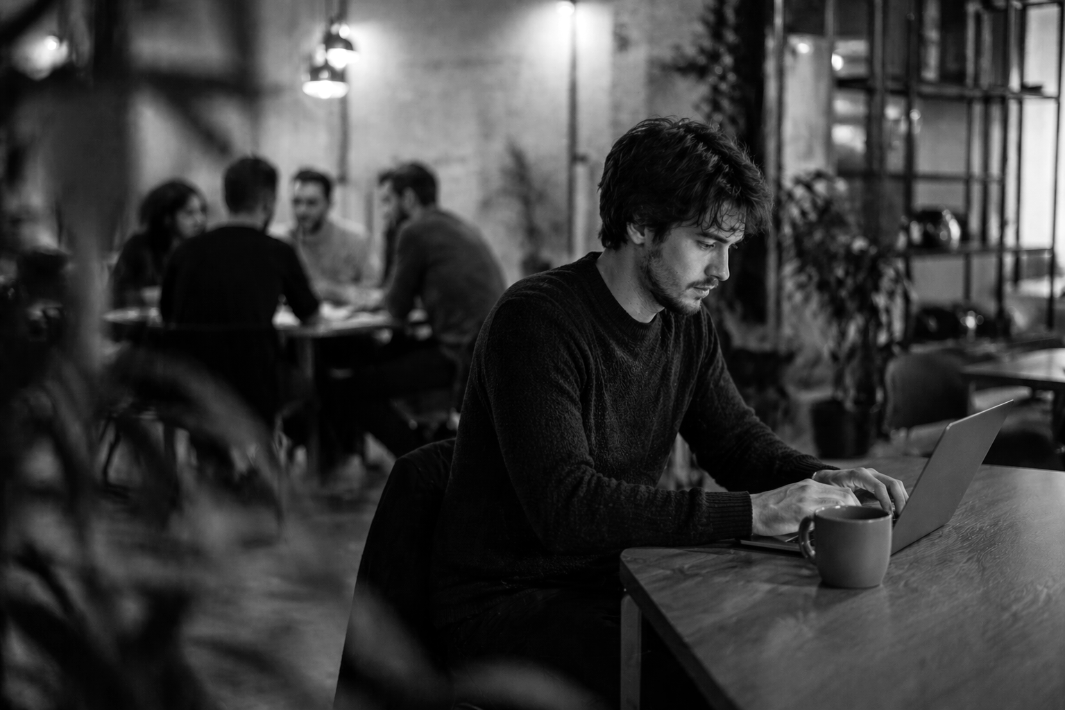 Black and white image of a man working at laptop in a modern office space.