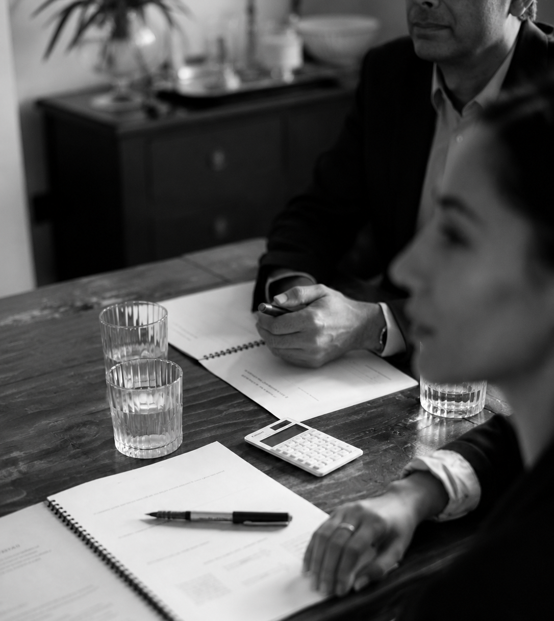 Black-and-white image of financial consultants reviewing documents and calculations during a meeting.