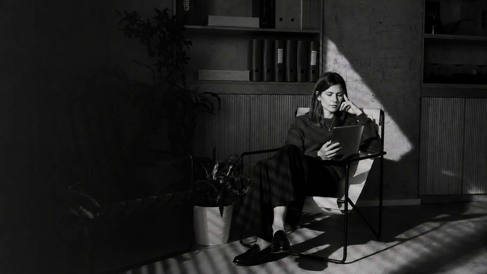 Woman sitting casually in home office space, holding a digital tablet.